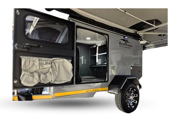 Close-up side perspective of the open side door on a grey Bush Lapa Shongololo caravan, highlighting the internal LED light, canvas storage pockets on the door frame, rugged off-road alloy wheel, and extended side awning.